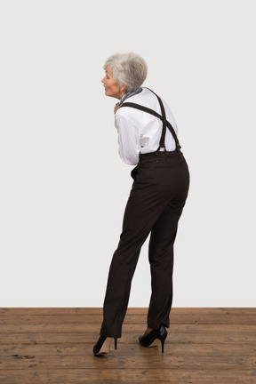 Dreiviertel-rückansicht einer alten dame in bürokleidung, die hände zusammenhält, während sie sich nach vorne beugt