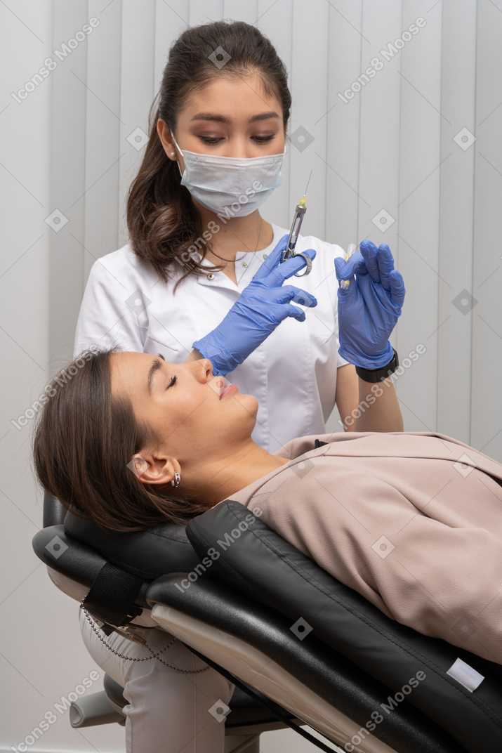 一位女牙医，拿着注射器和一名女病人，她闭着眼睛
