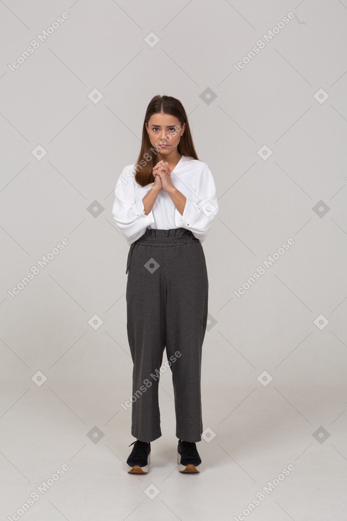 Front view of a sad young lady in office clothing holding hands together