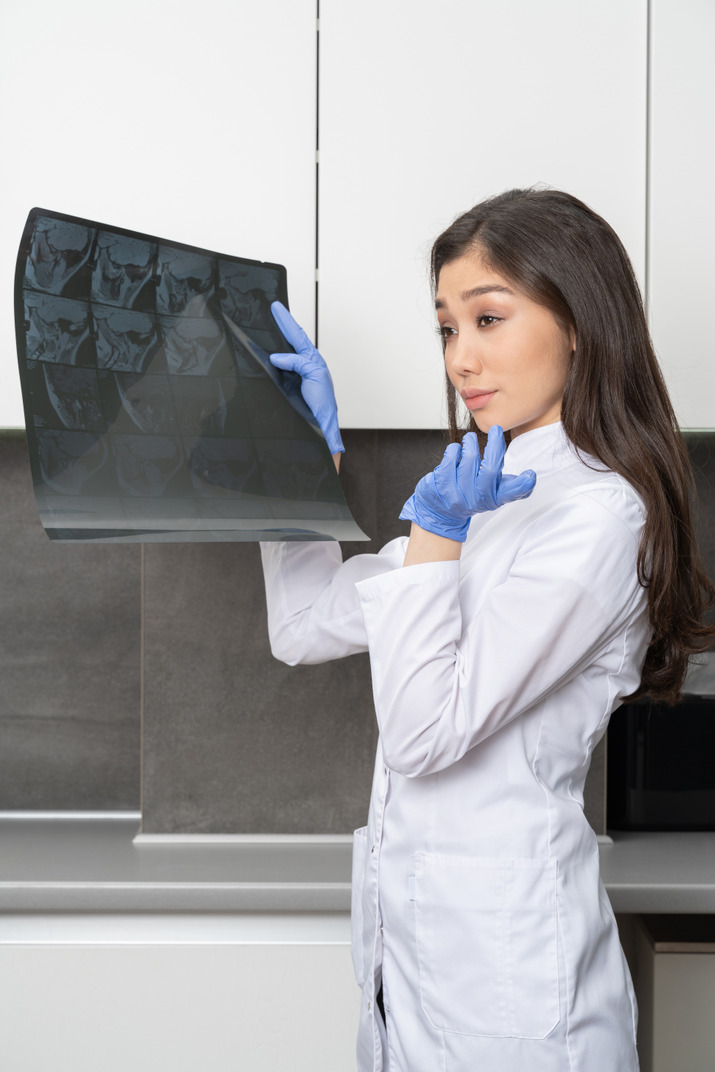 Side view of a puzzled female doctor holding an x-ray image and looking aside