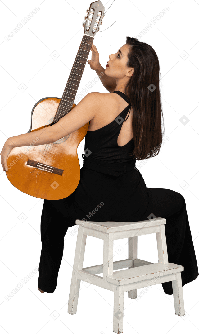 Vue arrière d'une jeune femme assise en costume noir touchant la tête de la guitare