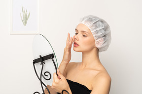 Jeune femme en casquette médicale levant le nez tout en regardant dans le miroir