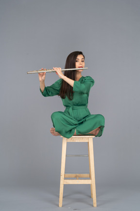 Comprimento total de uma jovem tocando clarinete sentada com as pernas cruzadas em uma cadeira de madeira