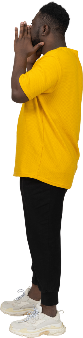 Vista lateral de um jovem de pele escura gritando em uma camiseta amarela