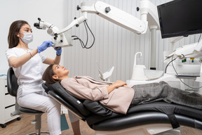 Pleine longueur d'une femme dentiste examinant sa patiente et regardant à travers le microscope