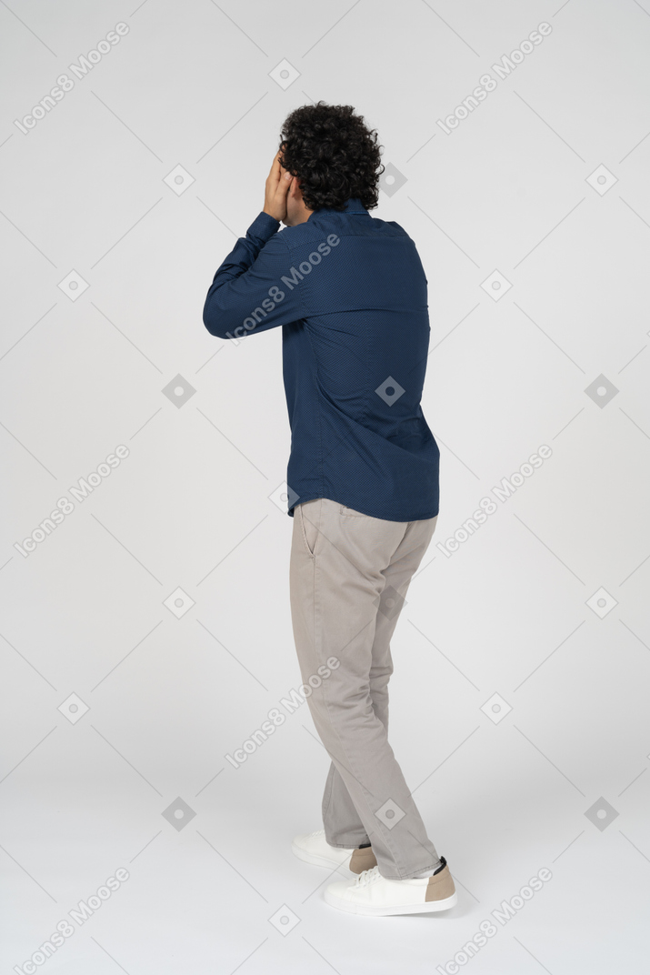 Rear view of a man in casual clothes covering face with hands