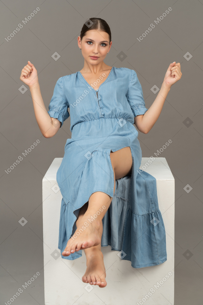 Vista frontal de una mujer joven sentada en un cubo y mirando a la cámara