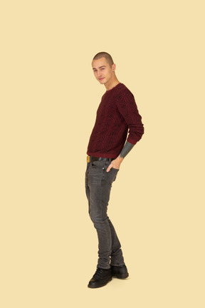 Vista laterale di un giovane uomo in pullover rosso che mette le mani nelle tasche posteriori