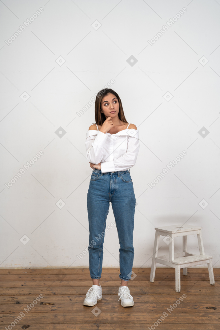 Woman in white blouse and jeans stands thinking