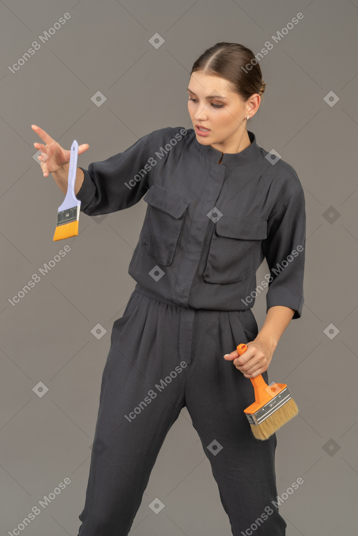 회색 작업복을 입은 여성이 페인트 브러시를 공중으로 던지고 있다