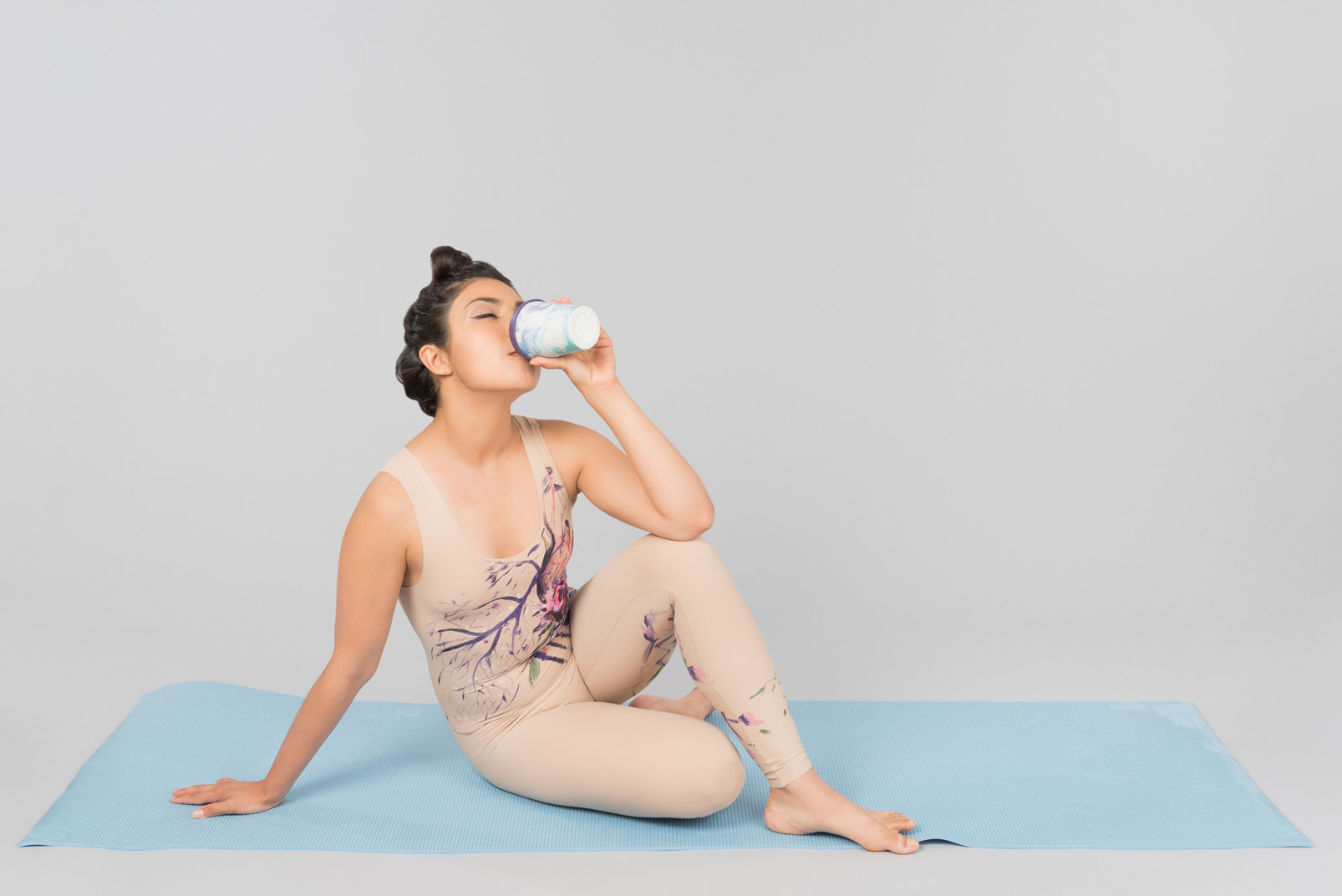 Young indian gymnast sitting on yoga mat and drinking coffee