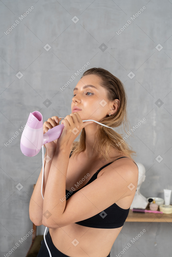Side view of a young woman winding a hairdryer cord around her neck