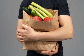 Jovem, abraçando um saco de papel com frutas e legumes