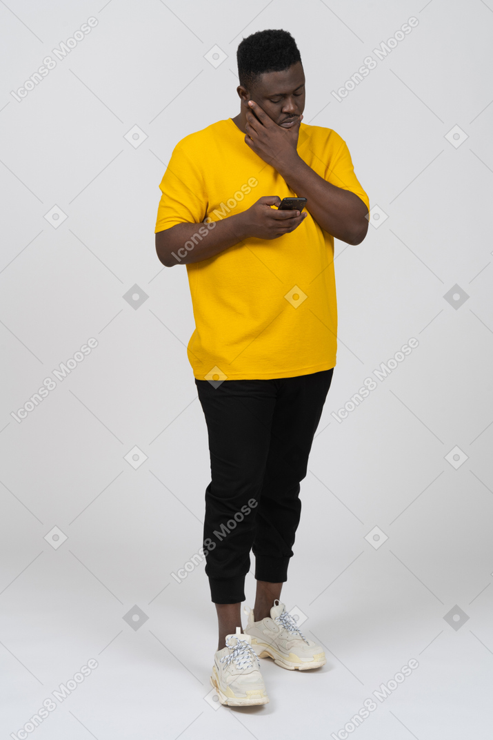 Vista frontal de un joven de piel oscura con camiseta amarilla charlando por teléfono