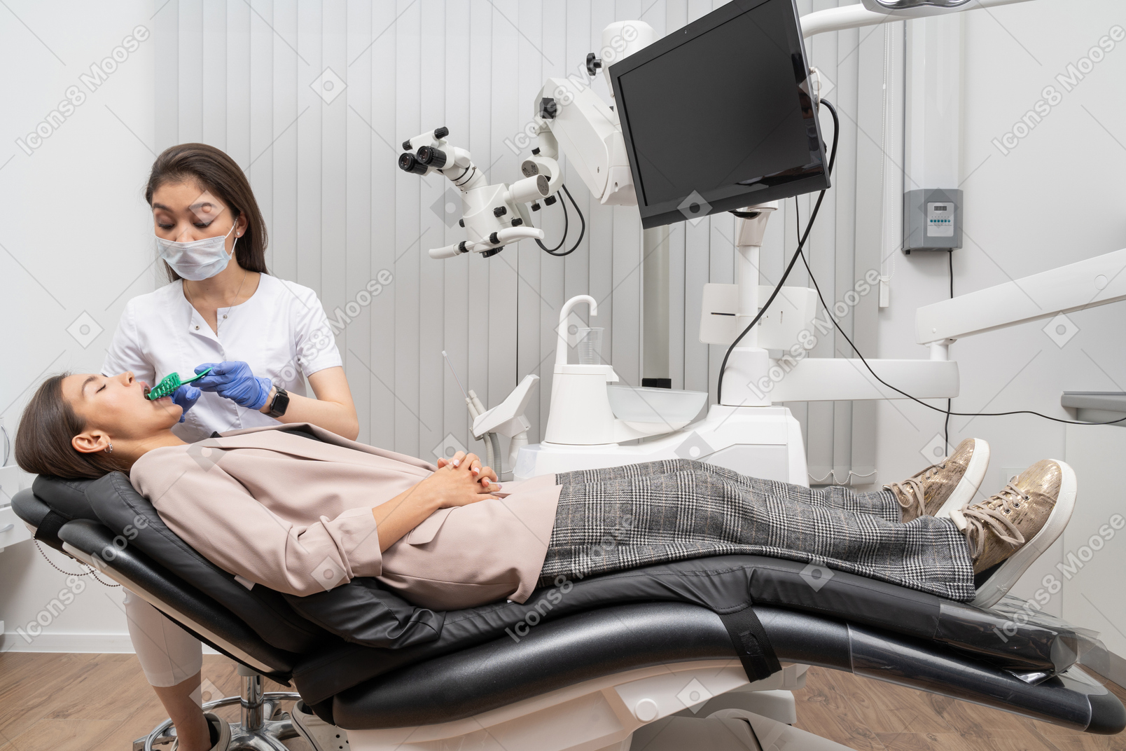 Женщина-стоматолог в полный рост делает стоматологическую запись своей пациентке в больничном кабинете