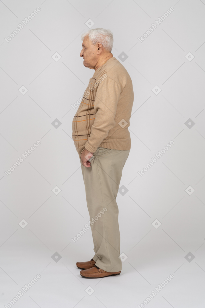 Side view of an old man in casual clothes standing with hands in pockets