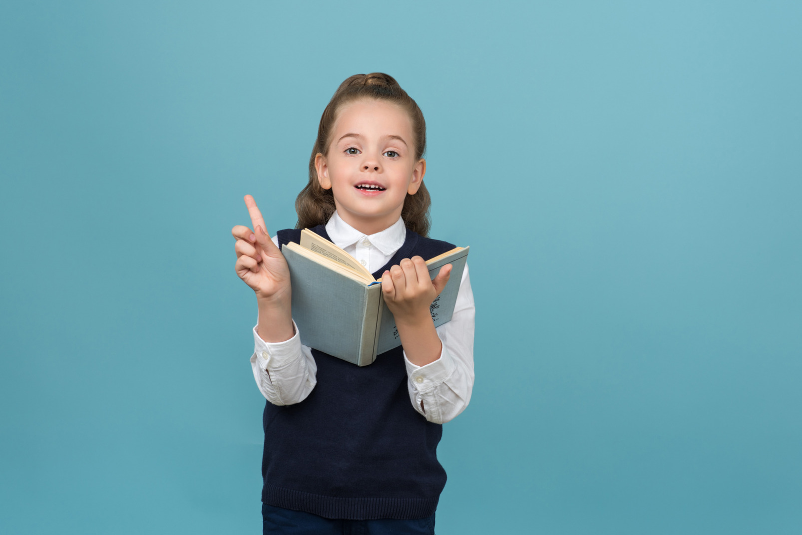 Primary schoolgirl holding an opened book and finger up