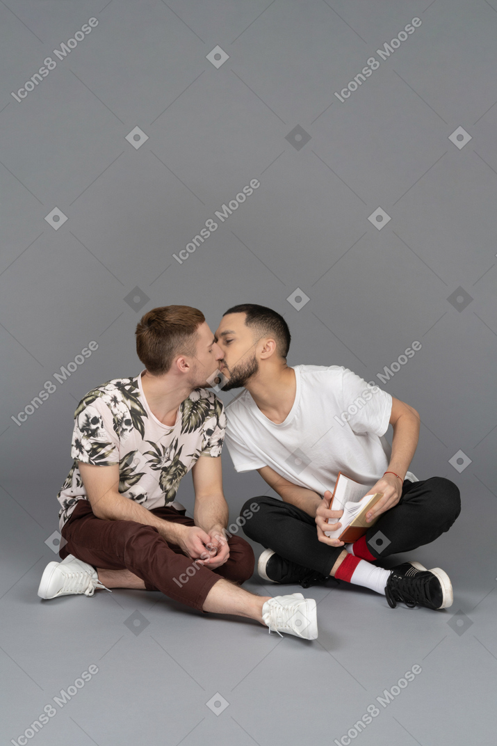 Front view of two young men sitting on the floor and kissing