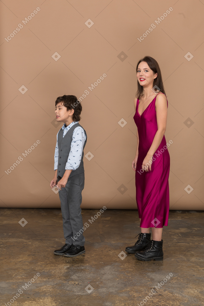 男の子が近くに立っている間カメラを見ている赤いドレスの女性