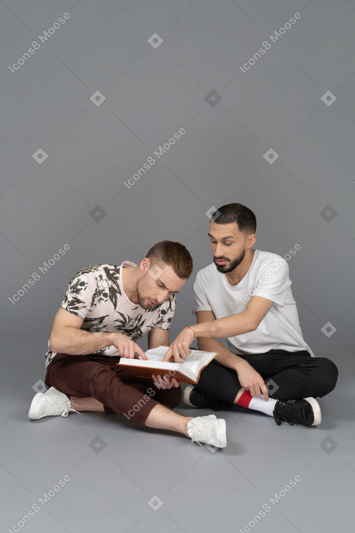 Vista frontale di due giovani uomini seduti sul pavimento e che studiano un libro