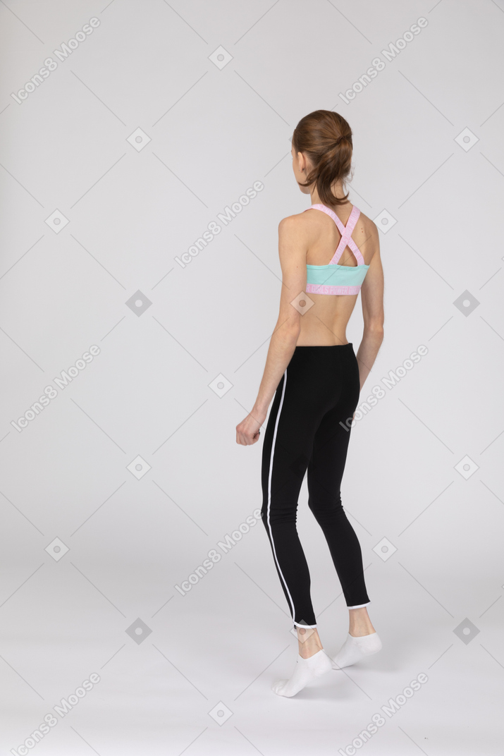 Vista laterale di una ragazza adolescente in abiti sportivi accovacciata e mettendo le mani sui fianchi