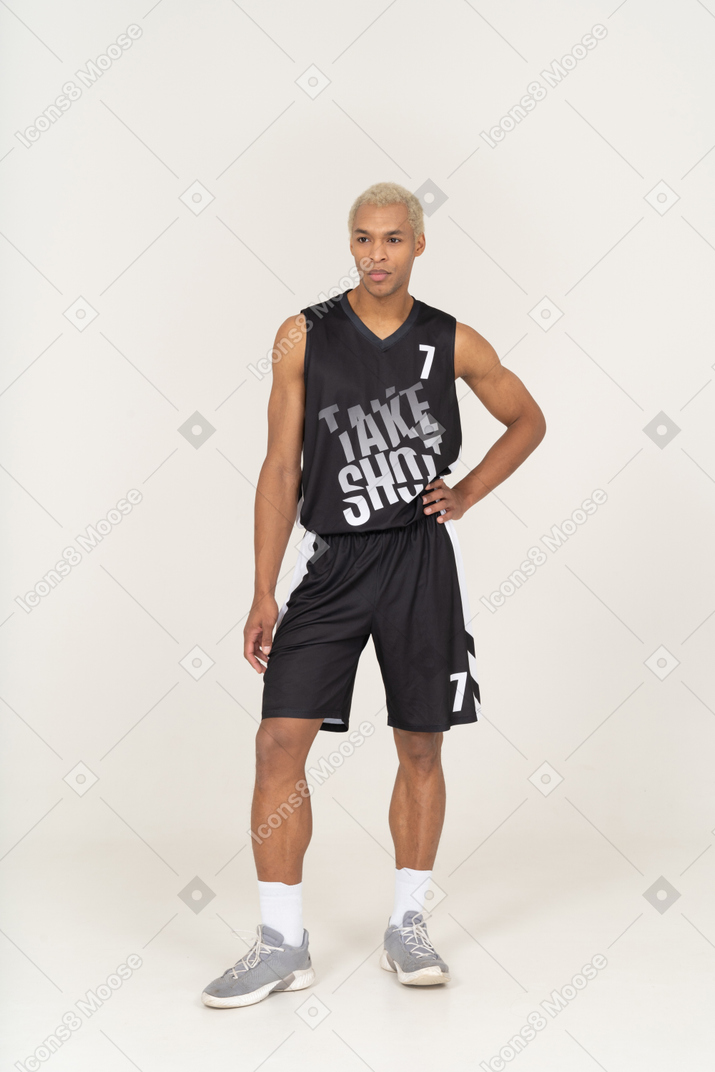 Vorderansicht eines jungen männlichen basketballspielers, der die hand auf die hüfte legt und in die kamera schaut