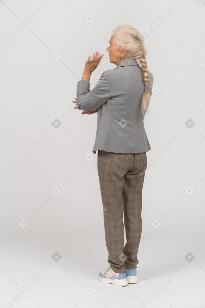 Вид сзади старушки в костюме, стоящей с поднятой рукой