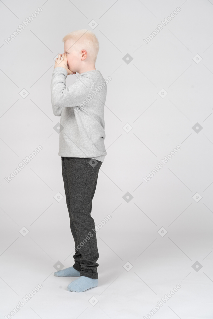 Vista lateral de un niño que cubre su boca con las manos