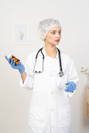 Vista frontal de uma jovem médica segurando um frasco de comprimidos