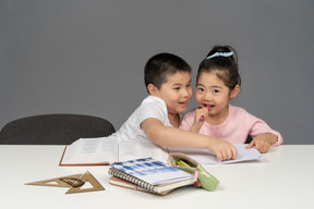 Брат и сестра улыбаются, делая домашнее задание