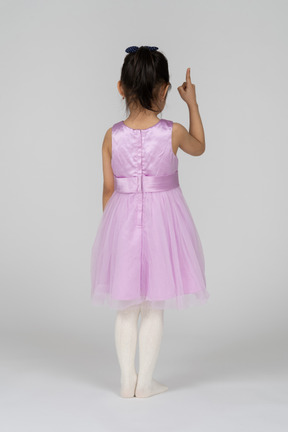Back view of a little girl in a cute dress pointing upwards