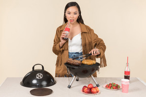 Joven mujer asiática preparando barbacoa y beber coca cola