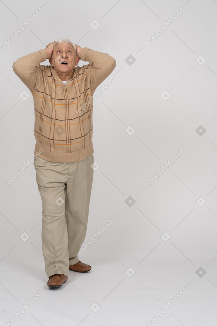 Vista frontal de un anciano impresionado de pie con las manos detrás de la cabeza