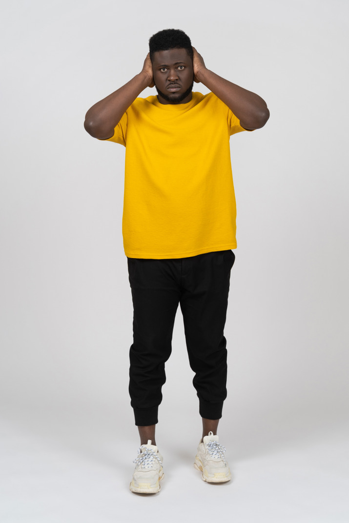 Front view of a dark-skinned man in yellow t-shirt blocking his ears