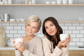 Two women holding coffee mugs in a kitchen
