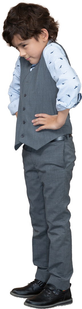 Seitenansicht eines süßen jungen im grauen anzug, der mit den händen auf den hüften posiert