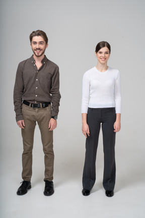 Vista de tres cuartos de una pareja joven sonriente en ropa de oficina