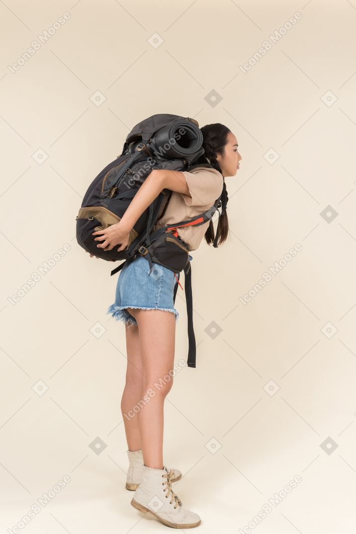Young female hiker carrying heavy backpack and standing back to camera