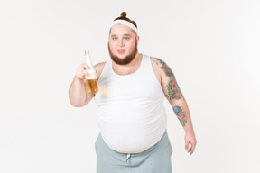 Толстый мужчина в спортивной одежде держит бутылку пива
