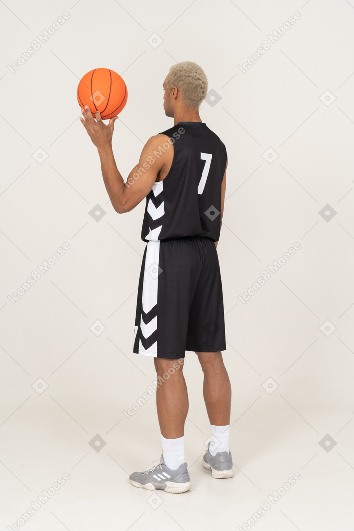 Vista posterior de tres cuartos de un joven jugador de baloncesto masculino sosteniendo una pelota