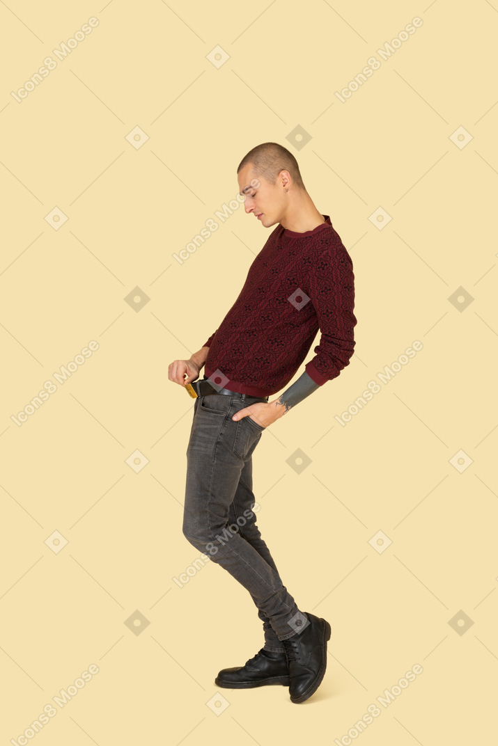 Вид сбоку на молодого человека в красном пуловере, касающегося пояса, откидываясь назад