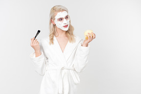 A good looking blond-haired young man in a white bathrobe, being in the process of his beauty care routine