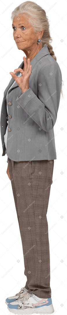 Vista lateral de una anciana en chaqueta gris mostrando signo ok