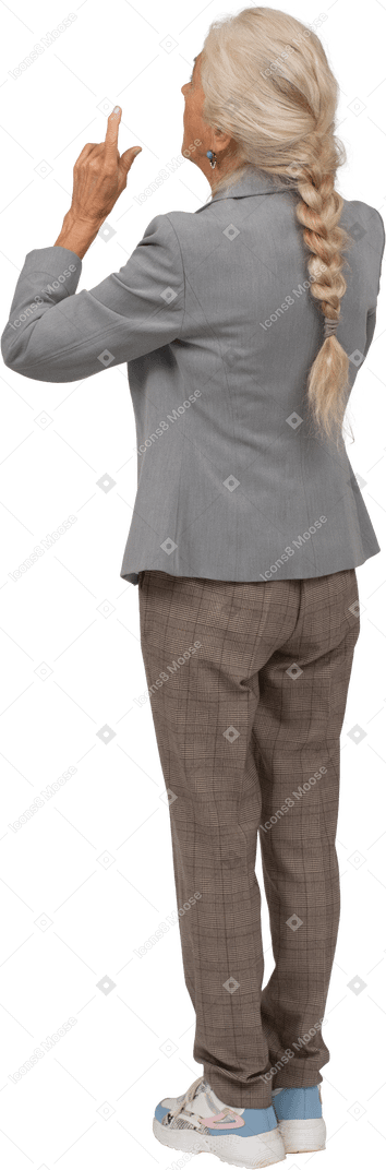 Vista trasera de una anciana en traje apuntando hacia arriba con el dedo