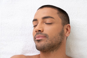 Handsome young man lying on white towel with his eyes closed