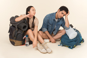 Jovem casal interracial sentado perto de mochilas enormes