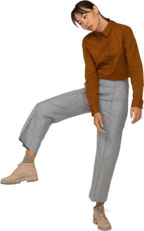 Vista frontal de una joven mujer asiática en calzones y blusa levantando la pierna