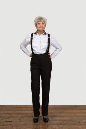 Front view of an old naughty female in office clothes bending down and grimacing putting hands on hips