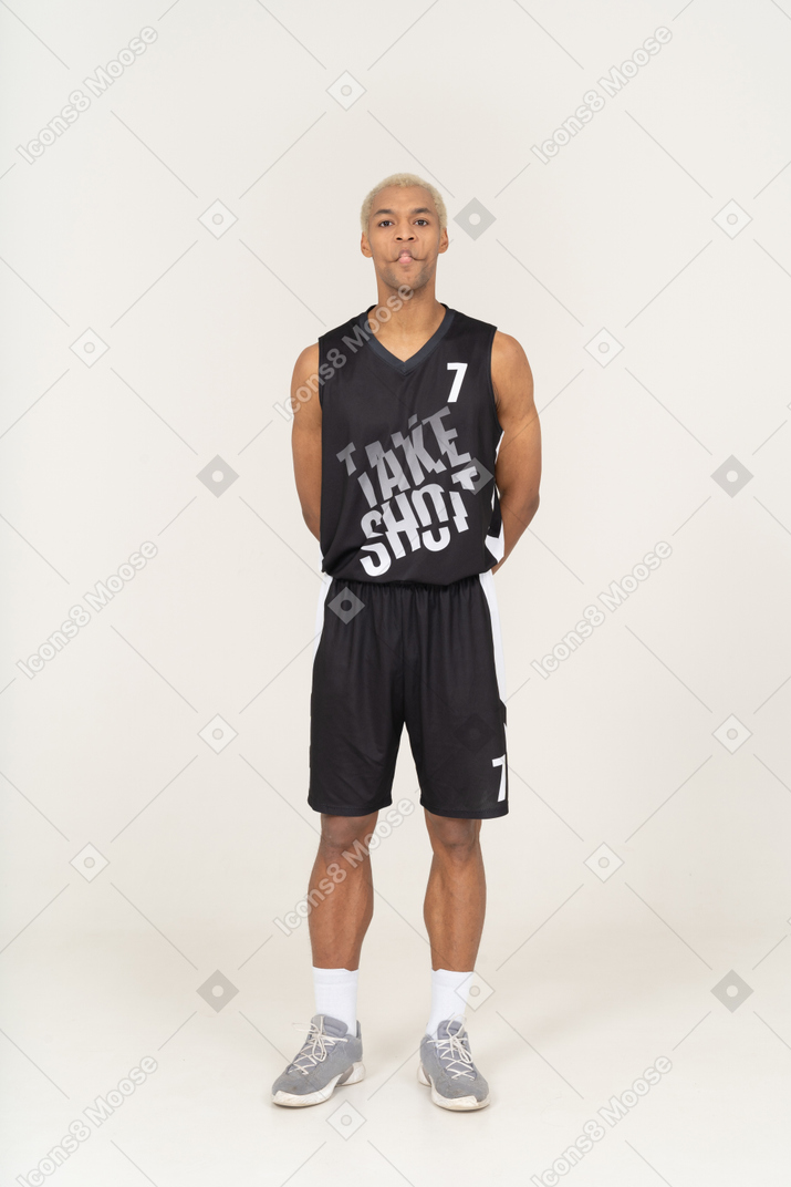 Vista frontal de um jovem jogador de basquete, mordendo os lábios e segurando as mãos atrás