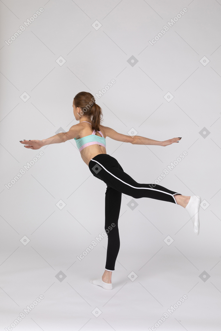 Three-quarter back view of a teen girl in sportswear balancing on her leg